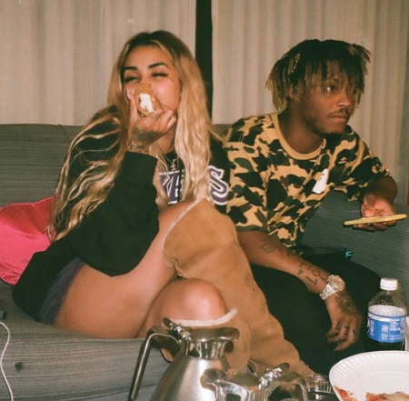 Juice Wrld and ally lottie sitting together. ally is eating cannoli and Juice Wrld is holding his phone looking at the other person in the room 
